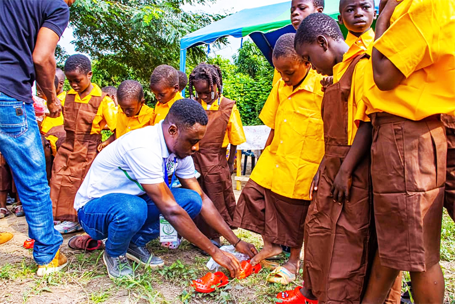 the ceo of as i grow assisting some of the children to put on their footwear and uniforms after the donation